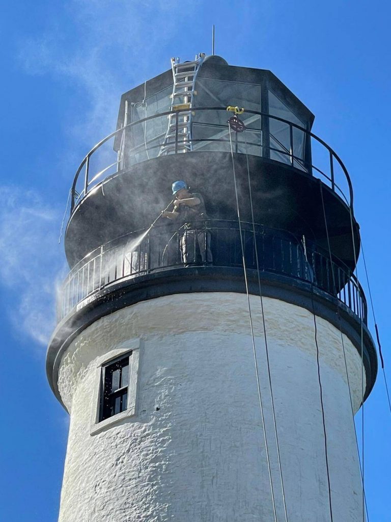 Worker power washing the top of the lighthouse