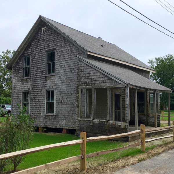 Shingled house with porch and split rail fence.