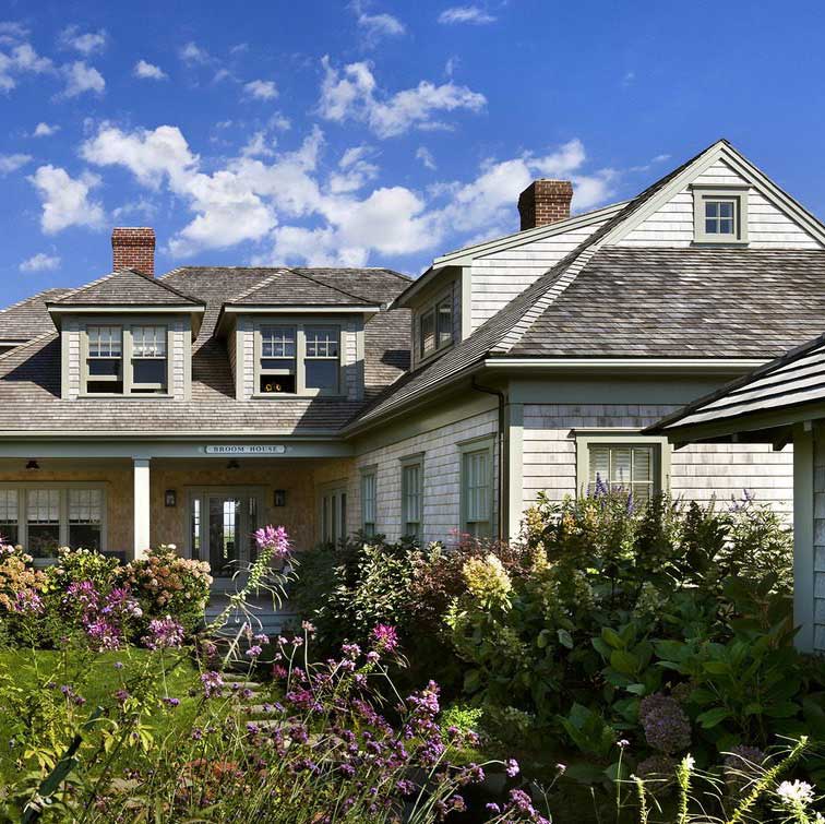 Cedar shingled house with a yard adorned with beautiful flowers.